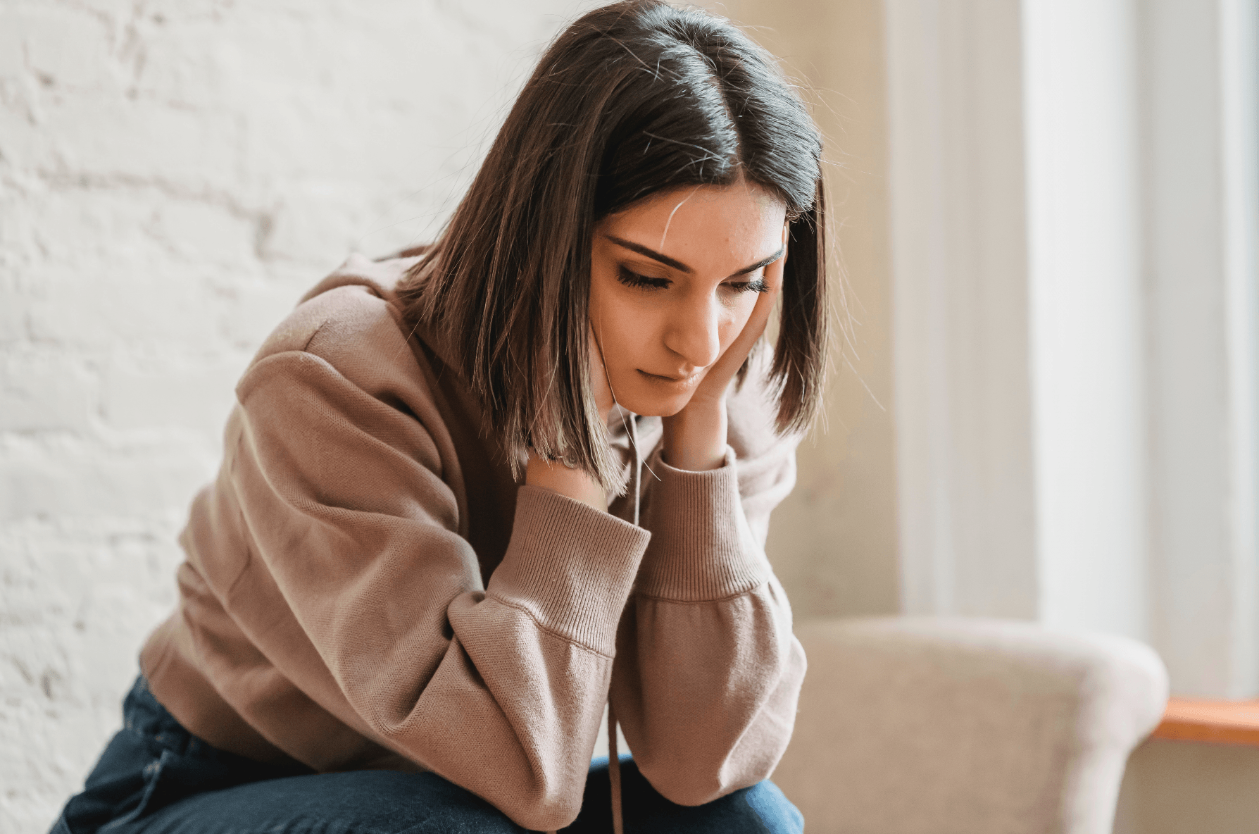 woman sitting looking down sitting wtih hands on face