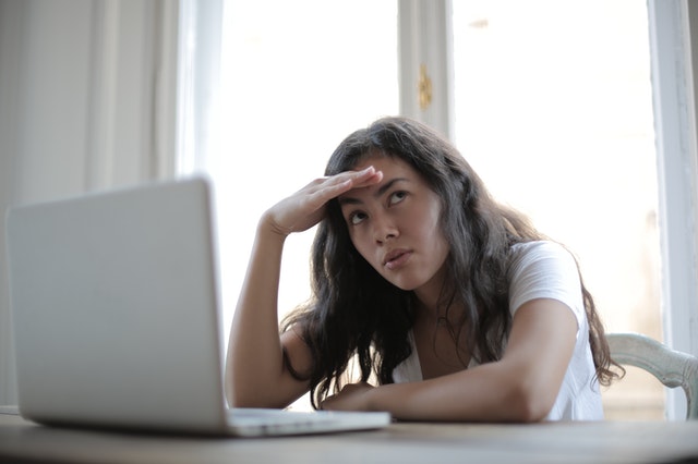 woman upset with hand on forehead on laptop in room