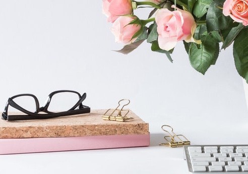 pink and white books with black glasses on top next to pink roses in vase