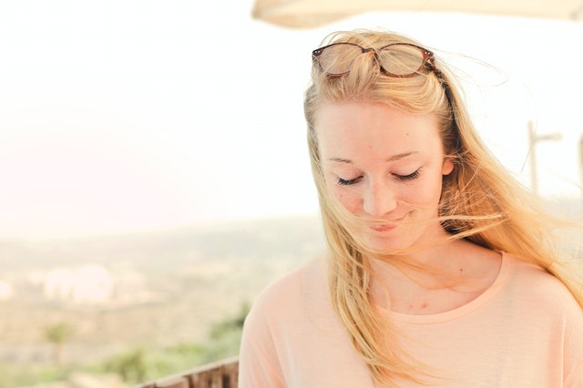 woman with peach colored top looking down with brown eyeglasses on her head